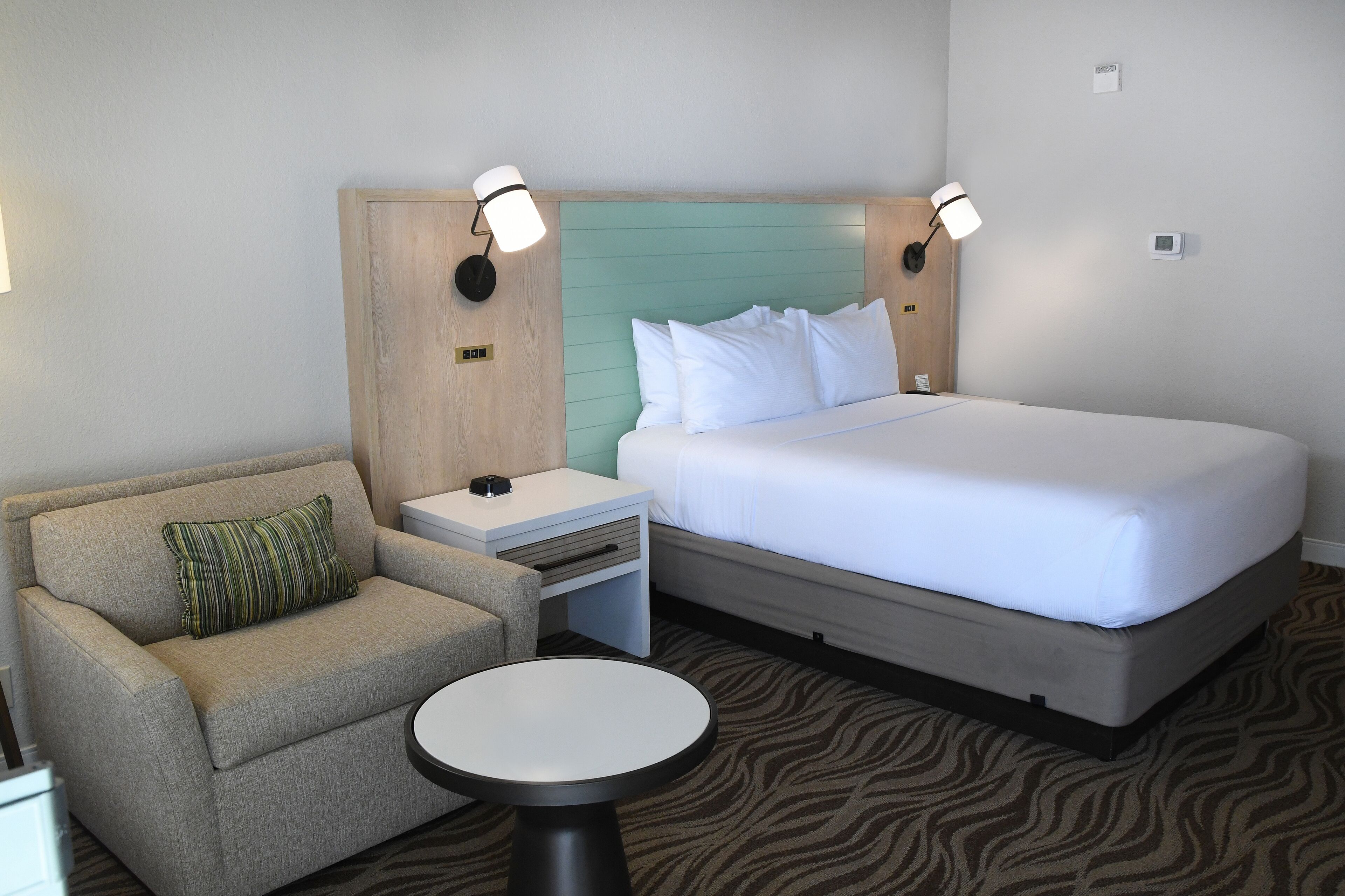 A hotel room with a bed, a sofa, a nightstand, and a small table.