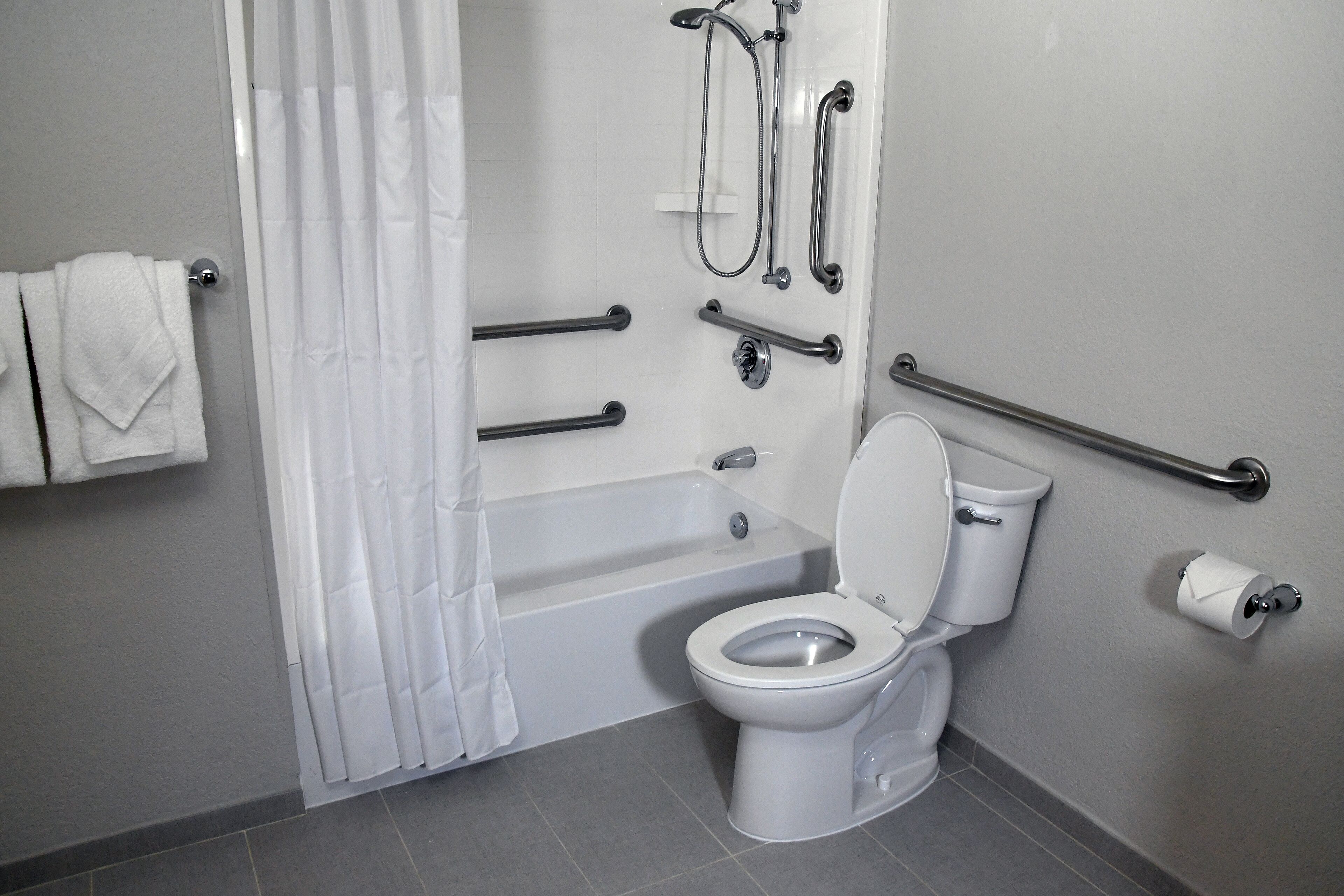 Ein Badezimmer mit einer Badewanne, Toilette und Haltegriffen.