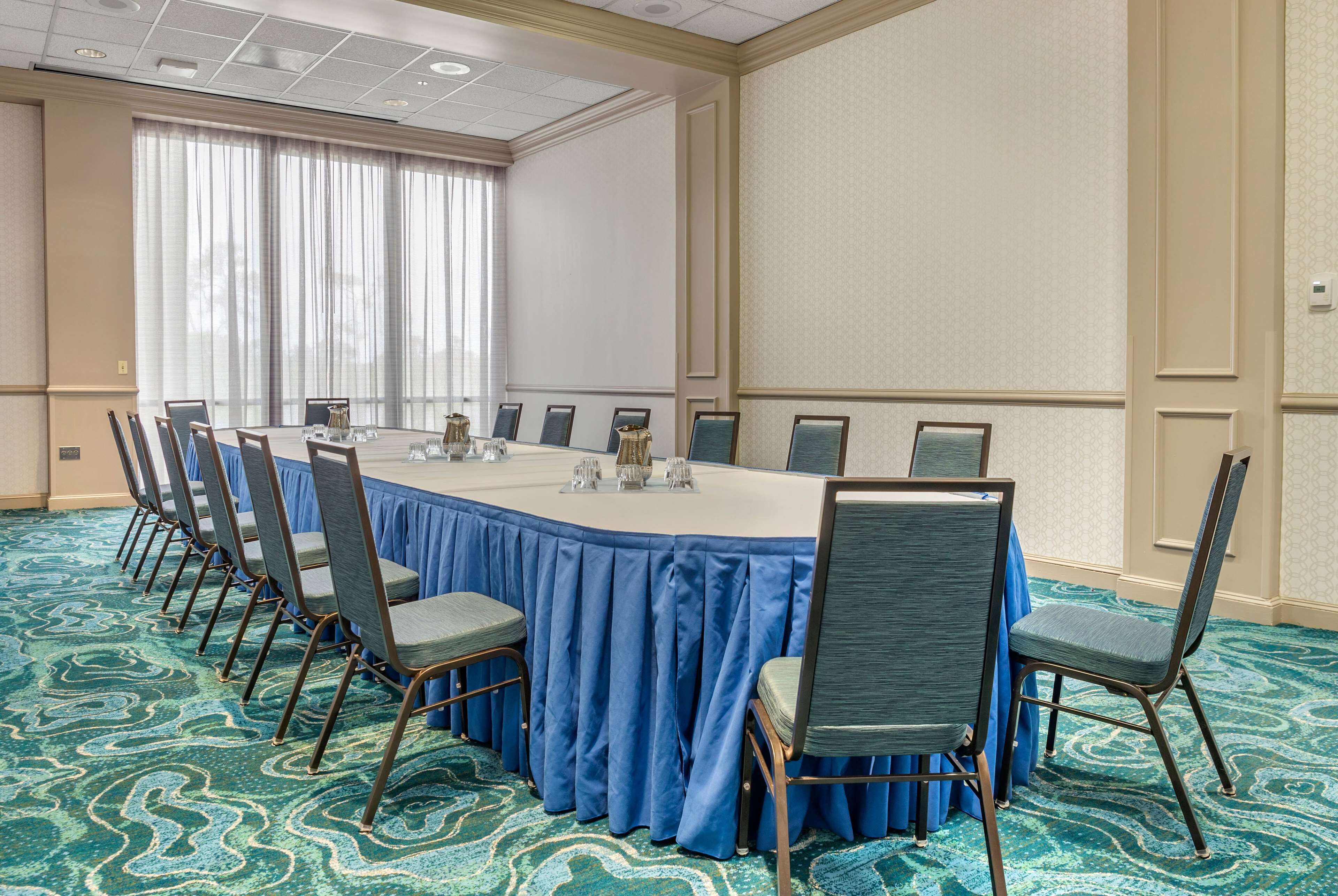 A conference room with a long table, blue chairs, and a patterned carpet.