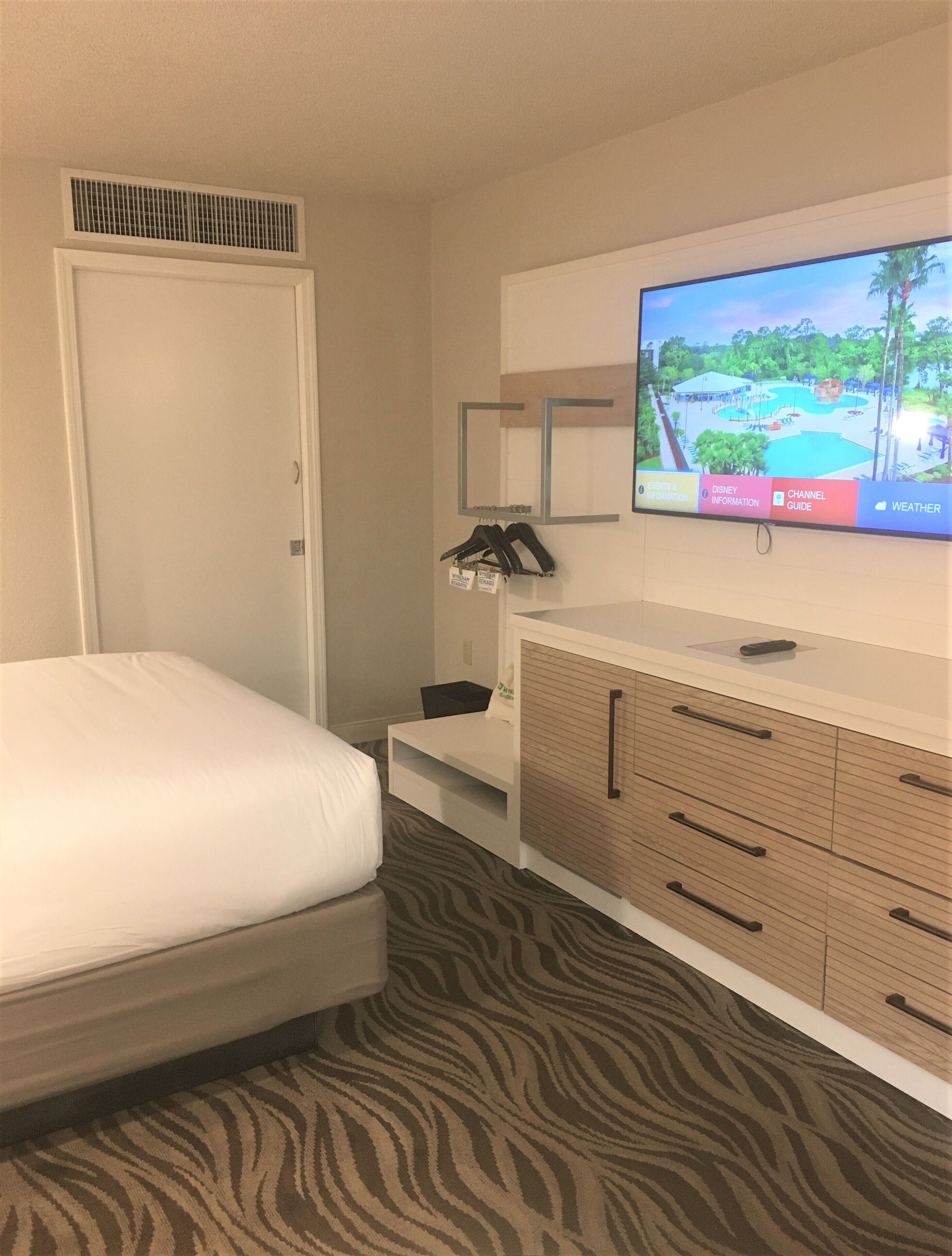 Een hotelkamer met een bed, een aan de muur bevestigde televisie, een bureau en een kledingkast.