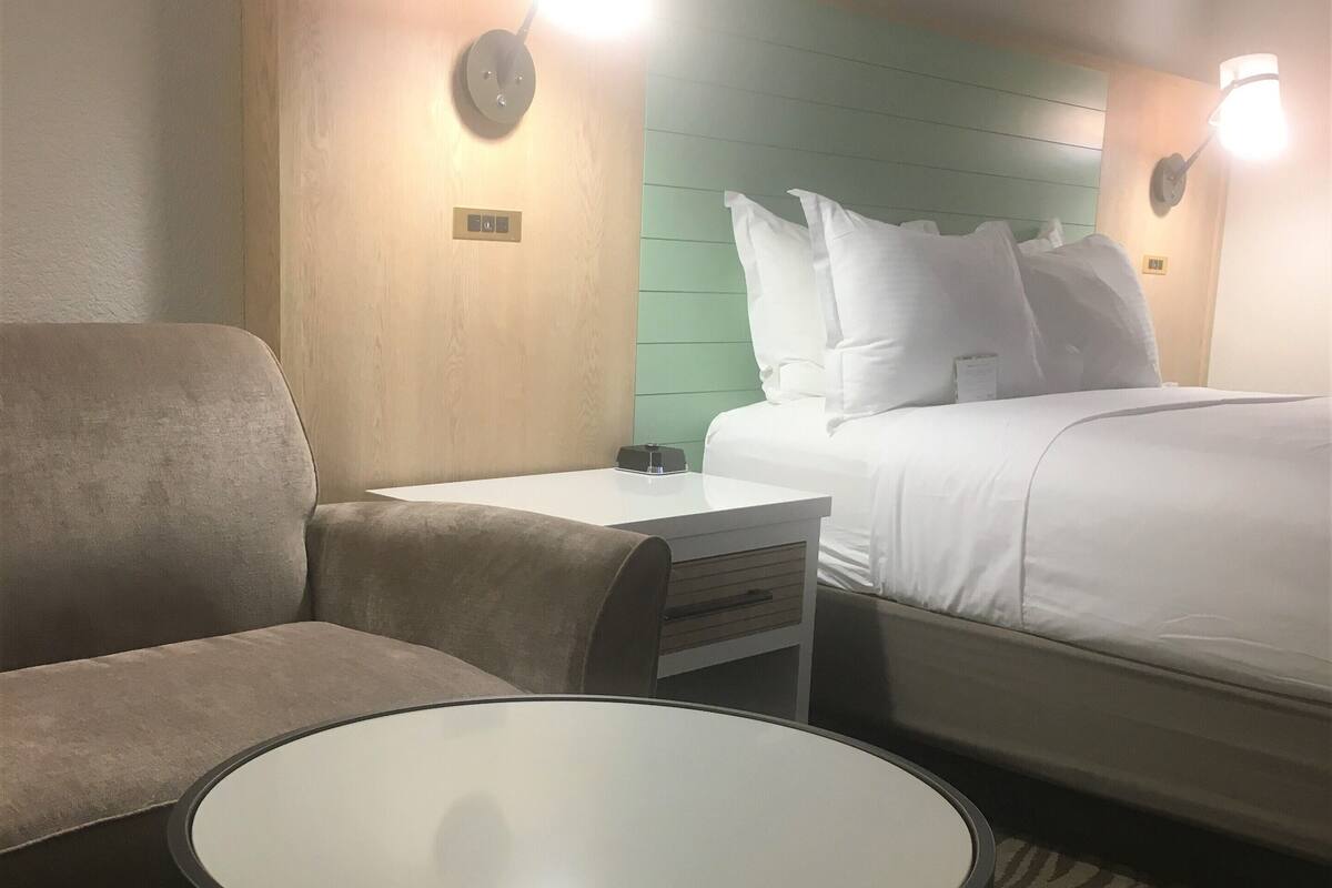 Et hotelværelse med en seng, en sofa, et lille bord og to væglamper.