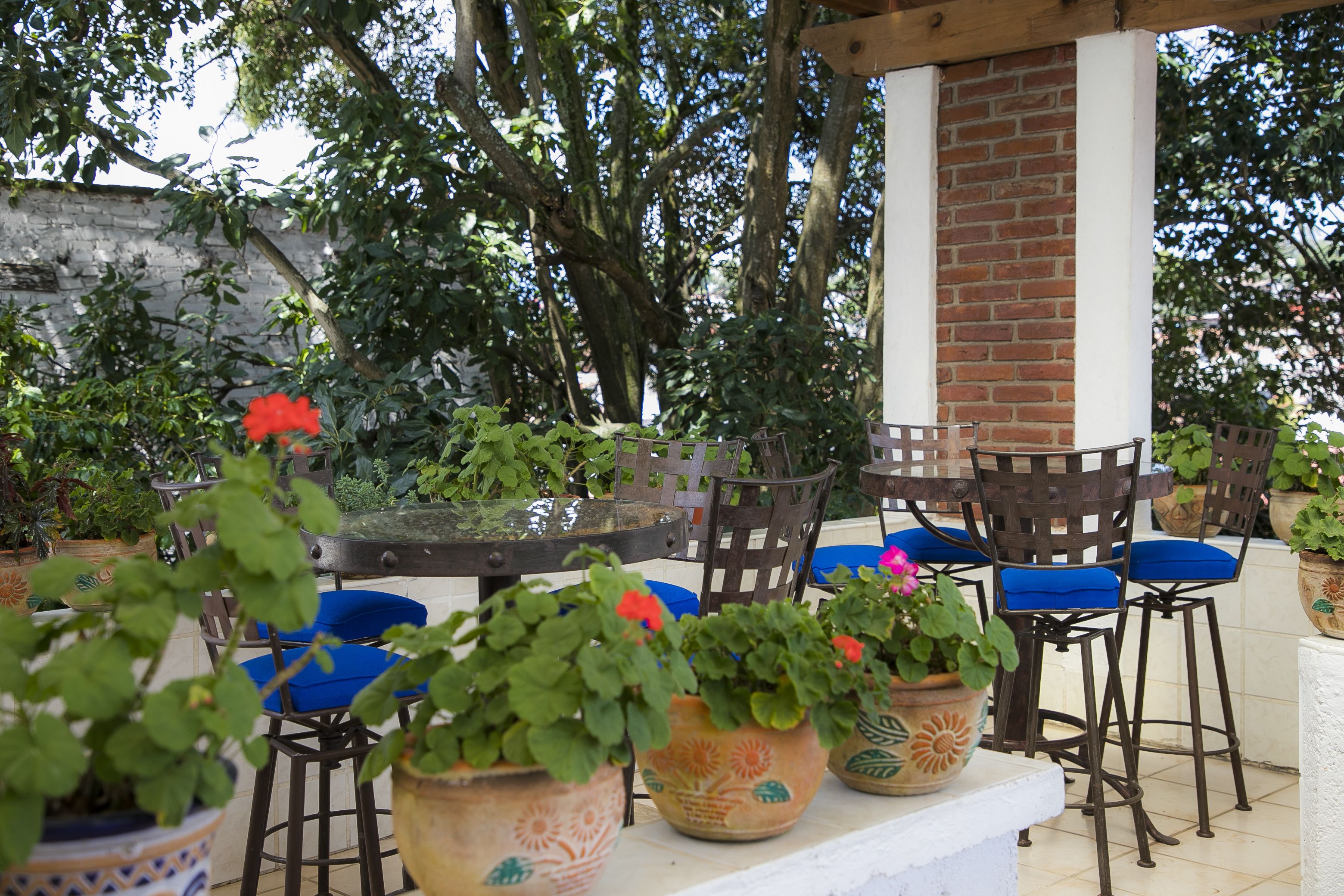 Un patio al aire libre con pared de ladrillo, sillas de madera y plantas en macetas.