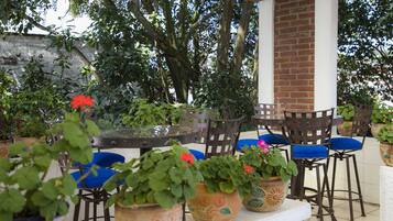 Un patio al aire libre con pared de ladrillo, sillas de madera y plantas en macetas.
