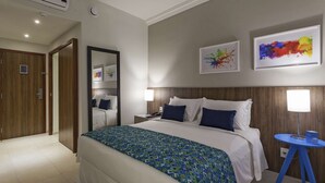 Habitación de hotel con una cama grande, una mesita de noche con lámpara, un espejo y dos obras de arte enmarcadas en la pared.