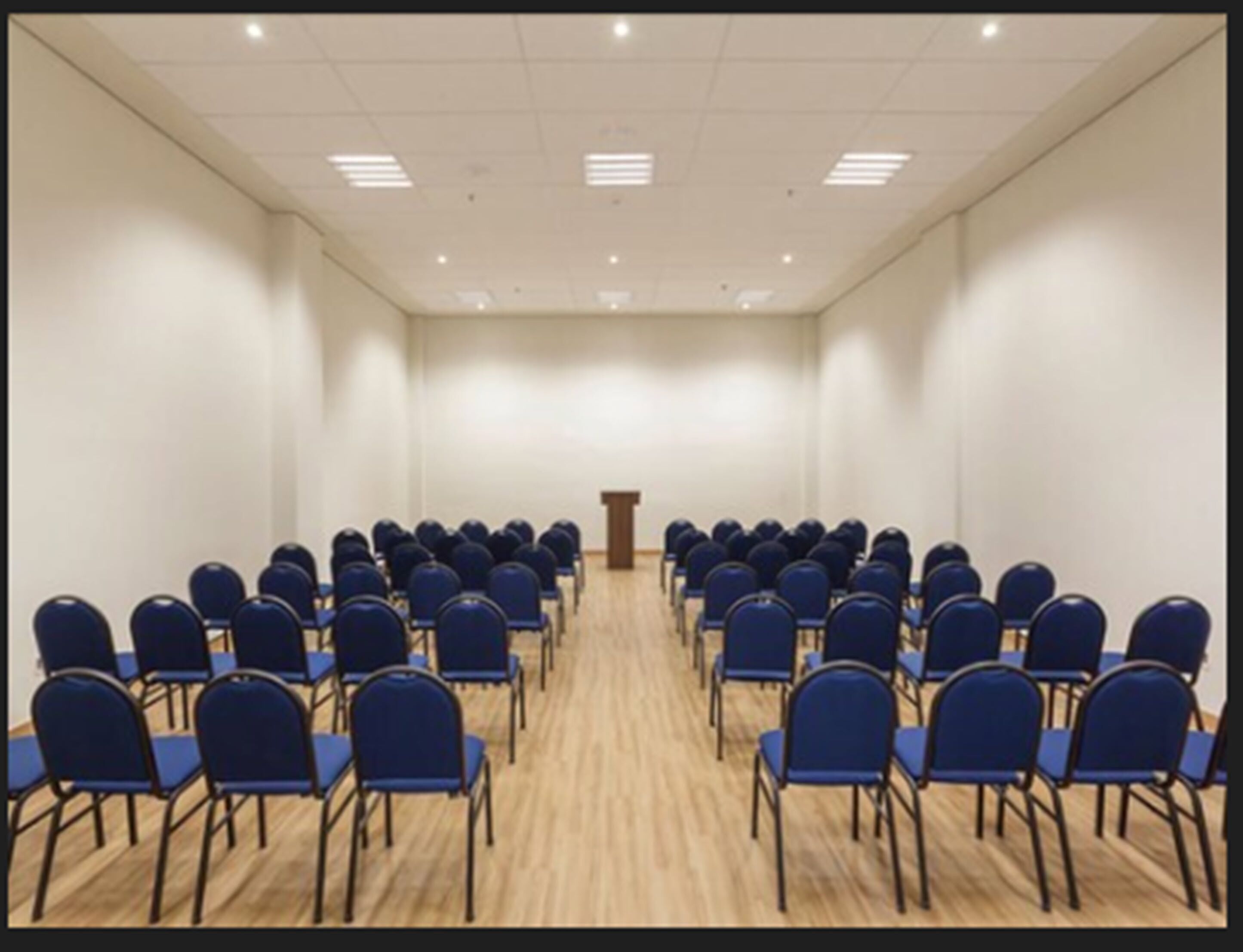 A conference room with rows of blue chairs facing a podium at the front.