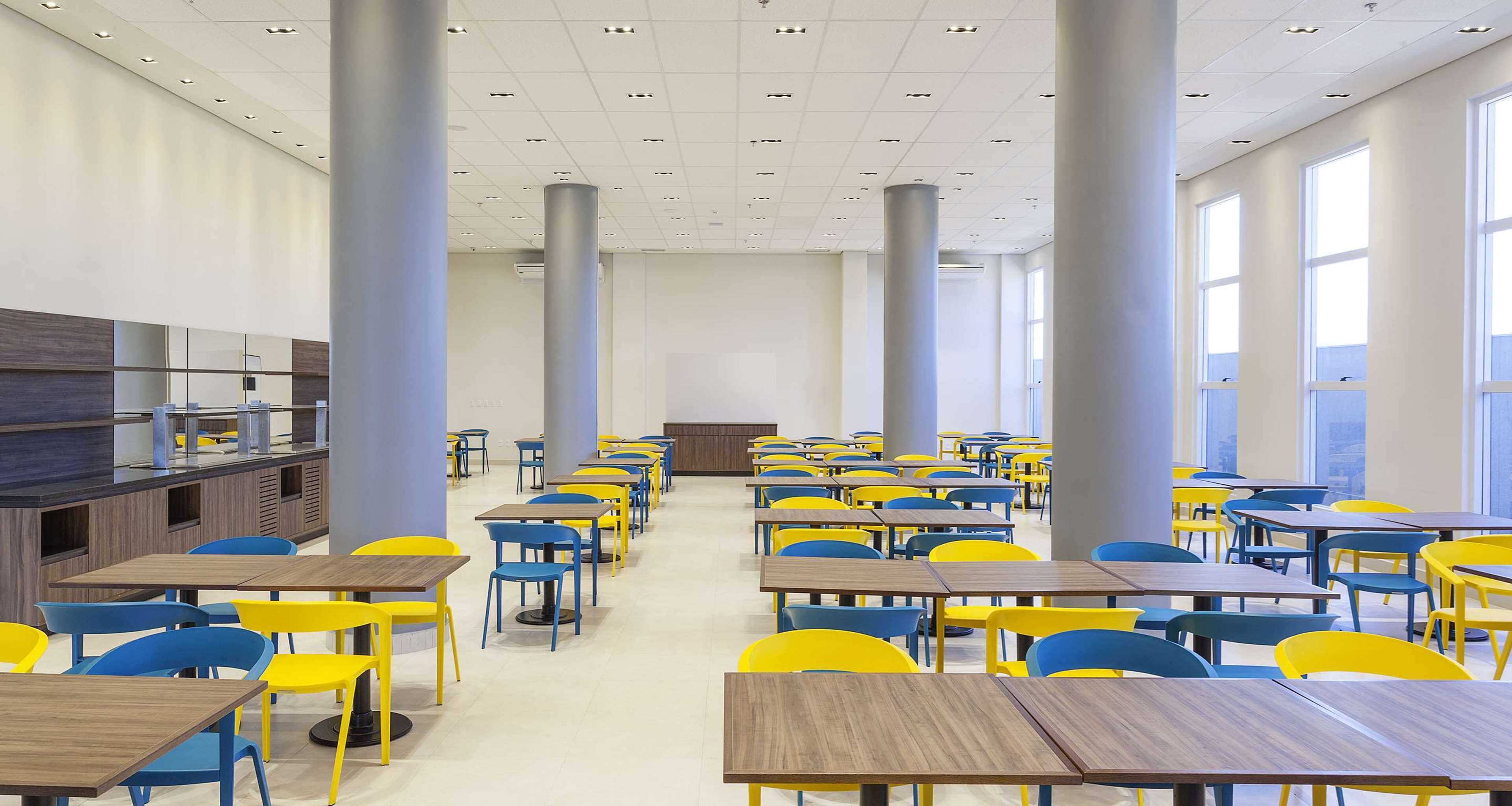 Une cafétéria spacieuse, dotée de hauts plafonds, de grandes fenêtres et d’un espace de service central.