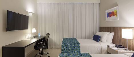 A hotel room with a desk, two beds, a TV, and a painting on the wall.