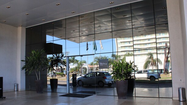 Una entrada de hotel moderna con puertas de cristal, plantas en macetas y una vista de coches aparcados y edificios al fondo.