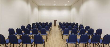 A conference room with rows of blue chairs facing a podium.