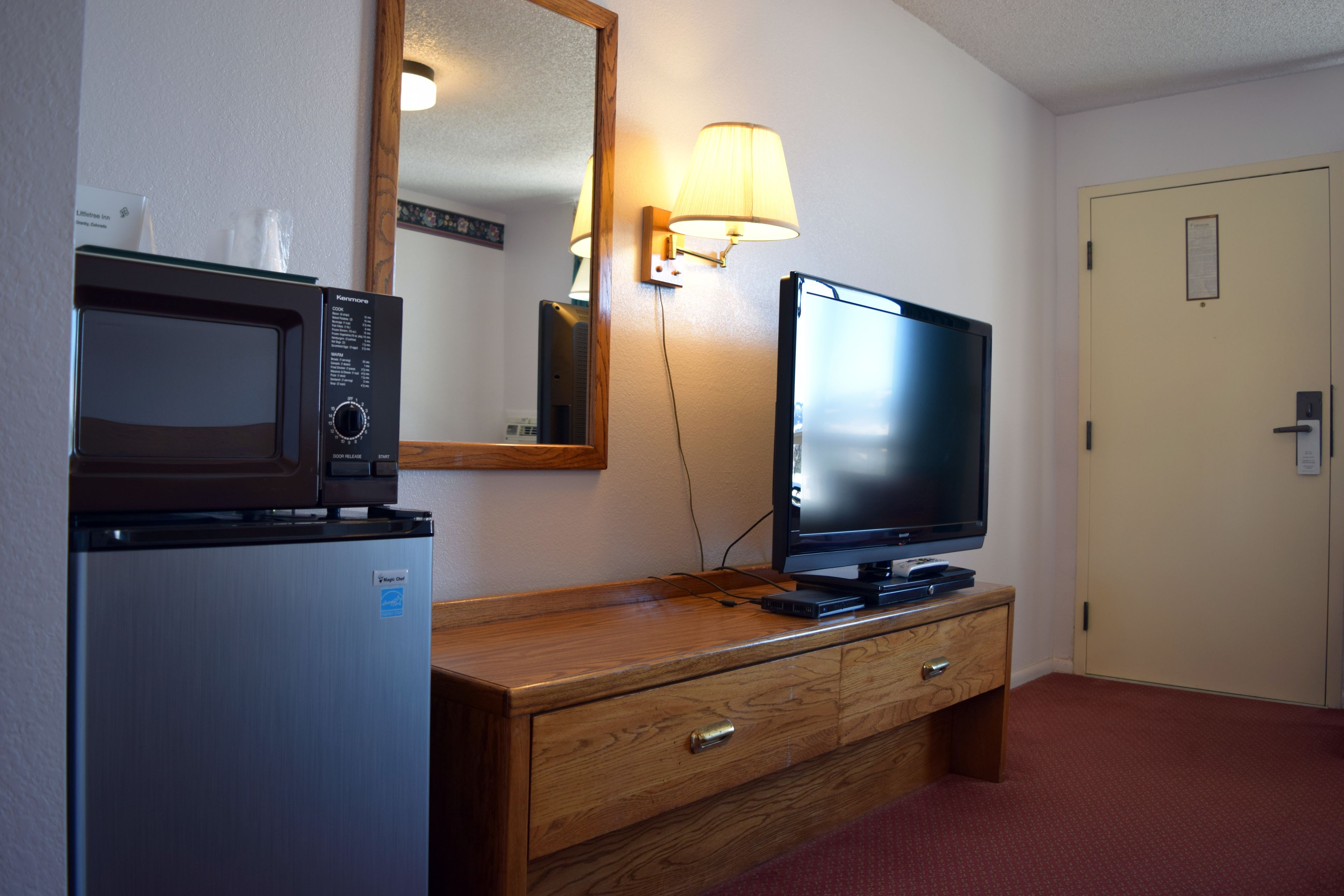 Habitació d'hotel amb un taulell de fusta, un microones, una televisió i una làmpada.