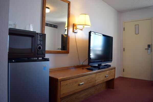 A hotel room with a wooden dresser, a microwave, a television, and a lamp. - Littletree Inn (Granby)