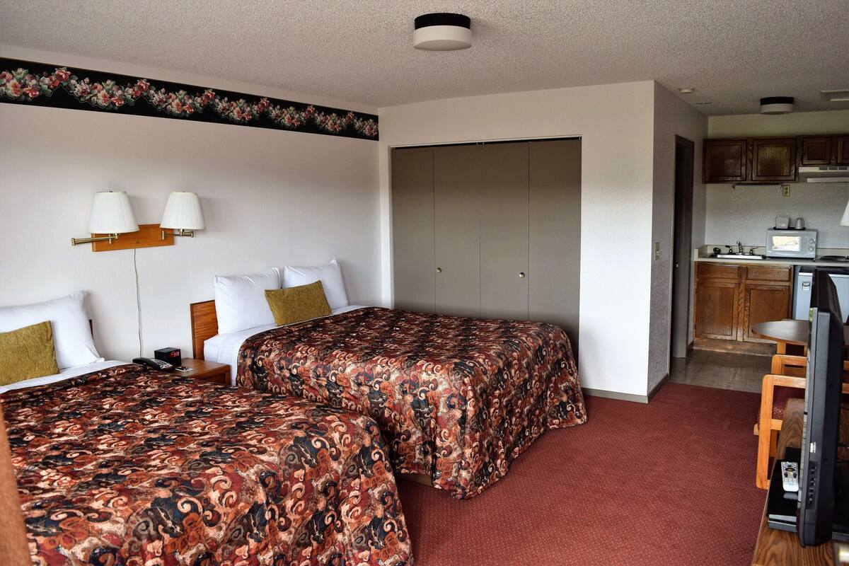 A hotel room with two beds, a kitchenette, and a bathroom visible through an open door.
