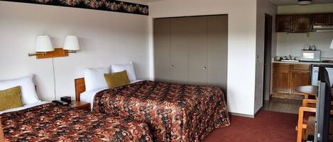 A hotel room with two beds, a kitchenette, and a bathroom visible through an open door.