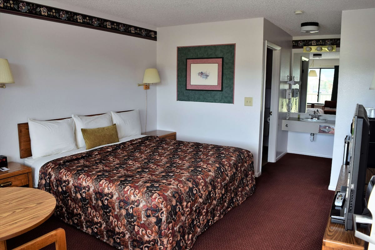 A hotel room with a large bed, a desk, a chair, a TV, and a bathroom visible through an open door.