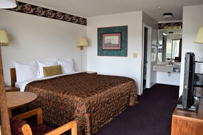 A hotel room with a large bed, a desk, a chair, a television, and a bathroom visible through an open door.