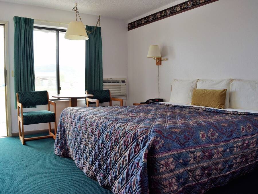 Quarto de hotel com uma cama, duas cadeiras, uma mesa e um abajur.
