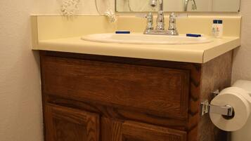 Ein Badezimmer mit Waschtisch aus Holz, einem Waschbecken, einem Spiegel, einem Fön und einem Toilettenpapierhalter.