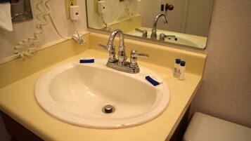 Un baño de hotel con un lavamanos blanco, un espejo y un inodoro.