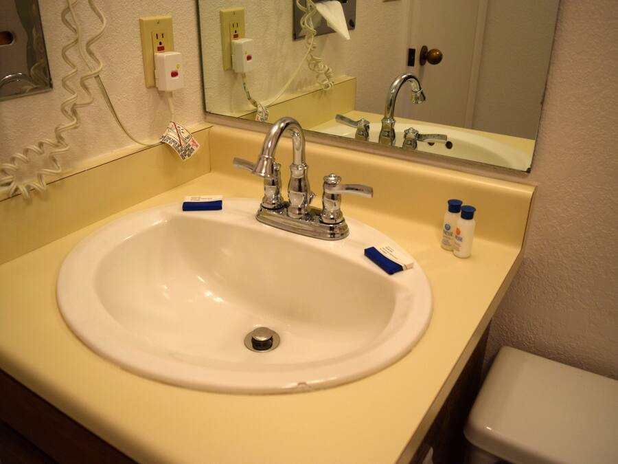 Un baño de hotel con un lavamanos blanco, un espejo y un inodoro.