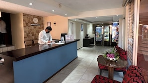 Zona de recepción de un hotel con un mostrador azul, un reloj y un área de descanso con sofás estampados en rojo y negro.