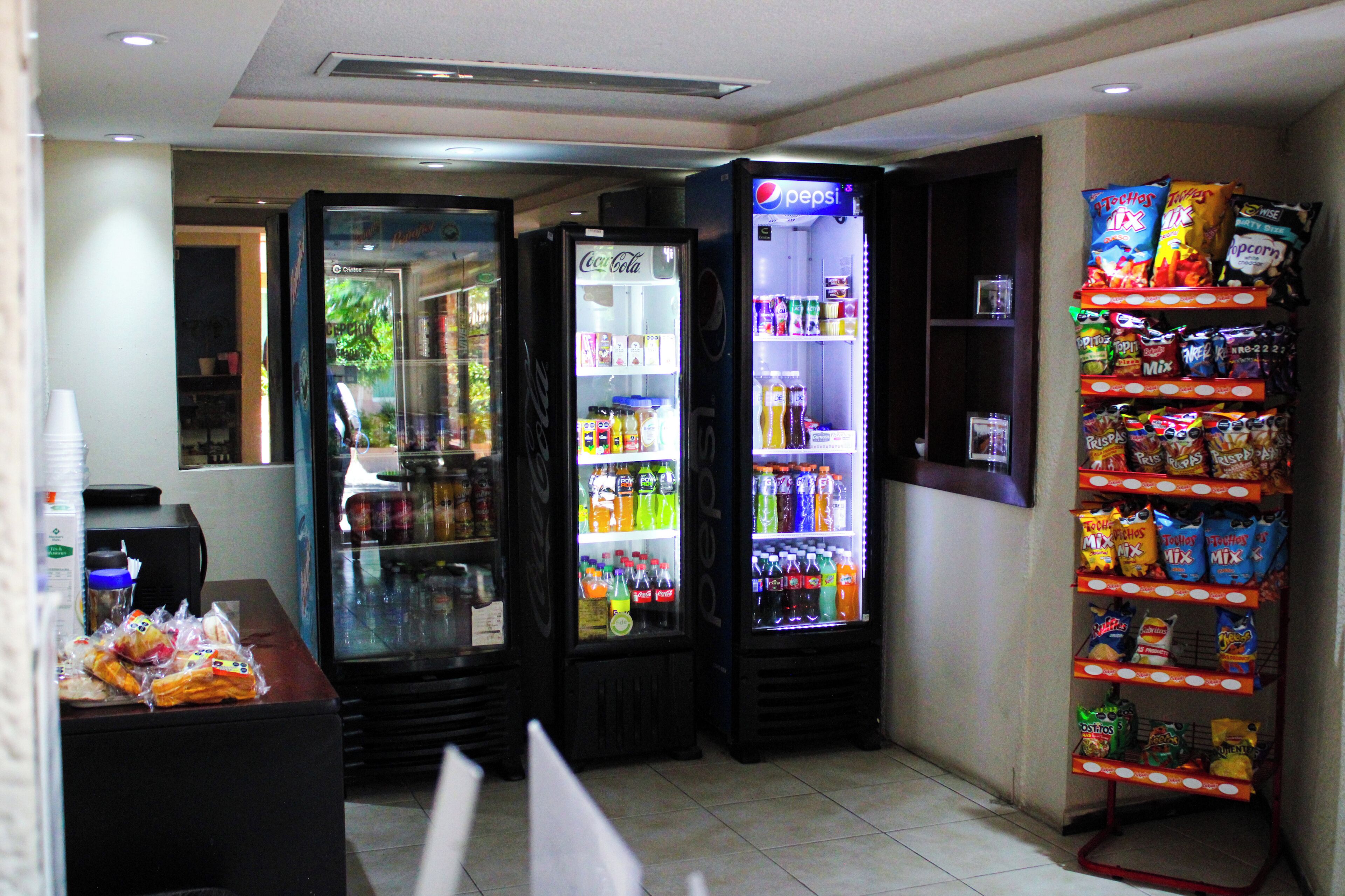 Zona de venta automática con refrigeradores de Pepsi y Coca-Cola, dispensadores de aperitivos y una variedad de bebidas.