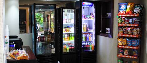 Zona de venta automática con refrigeradores de Pepsi y Coca-Cola, dispensadores de aperitivos y una variedad de bebidas.