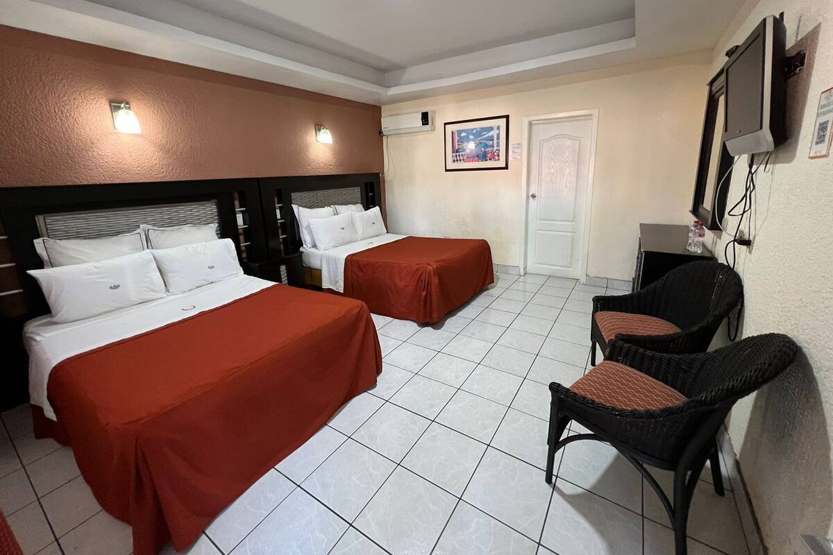 A hotel room with two beds, a television, a chair, and a door.