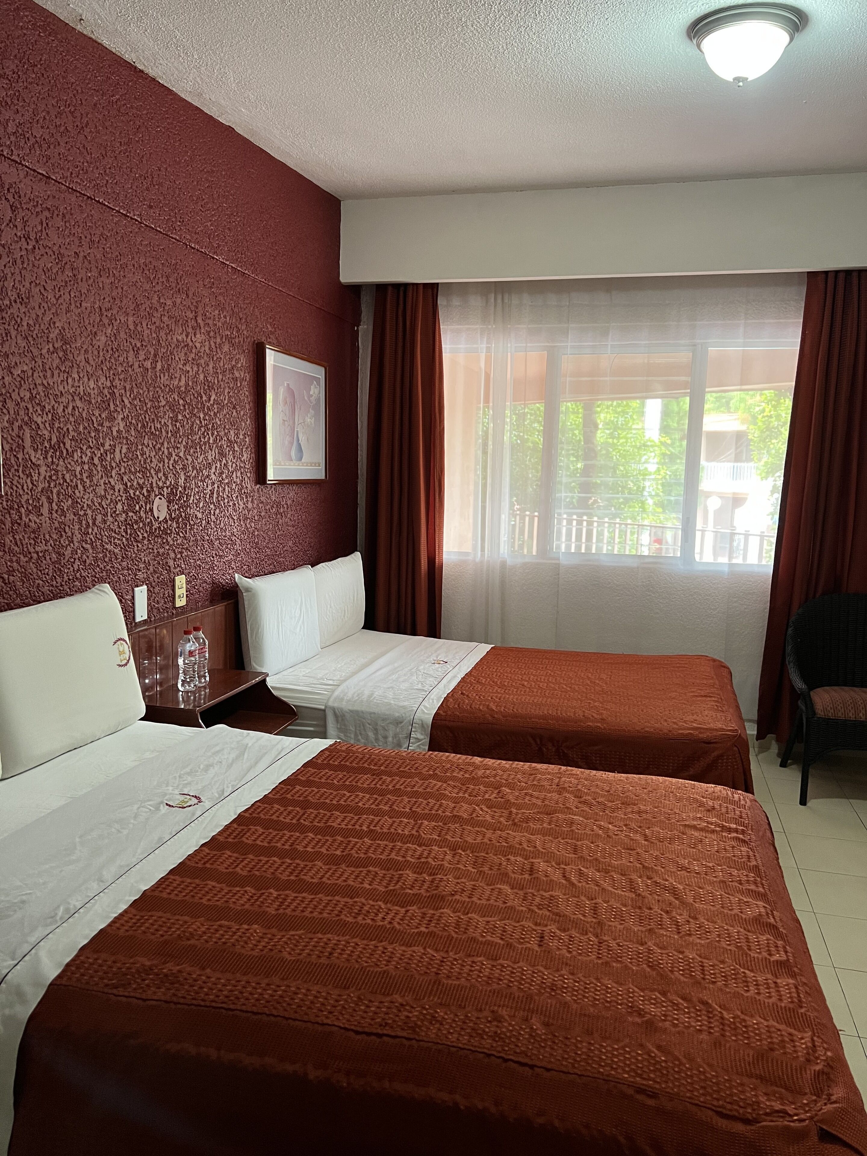 Habitación de hotel con dos camas, cabecera de madera, un cuadro en la pared y una ventana con cortinas.