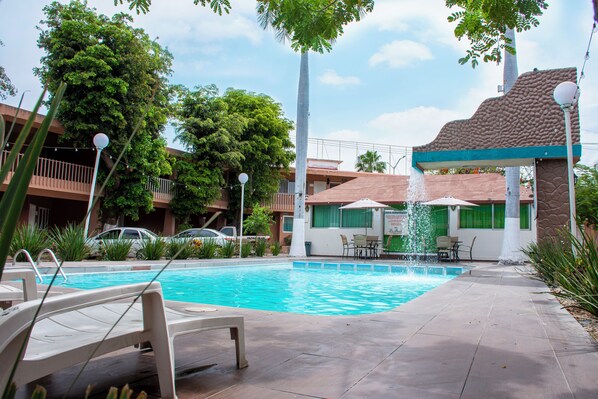 Una piscina con sillas de descanso, un elemento acuático y un edificio de fachada de piedra.