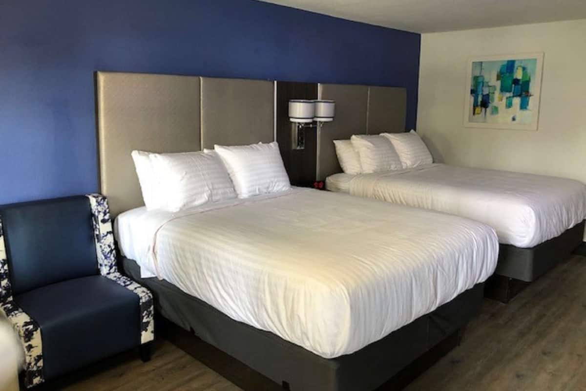 A hotel room with two beds, a sofa, and a painting on the wall.