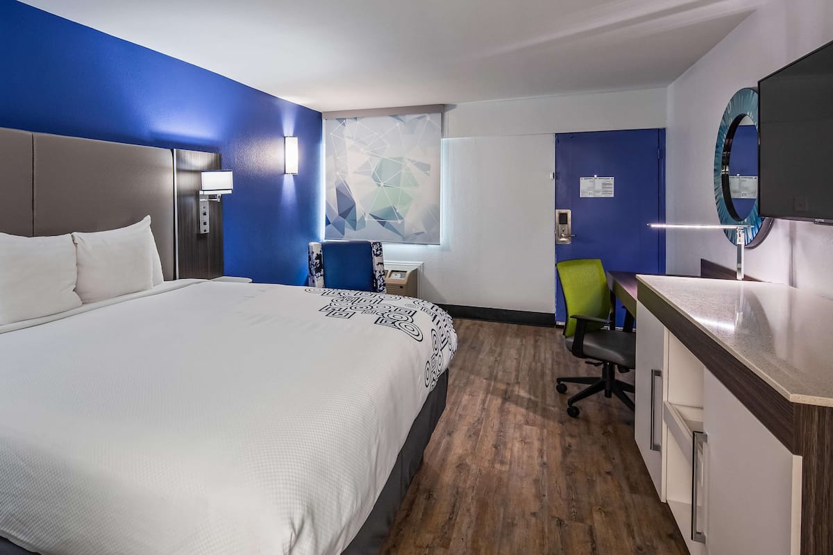 A hotel room with a large bed, a desk, a chair, and a mirror.