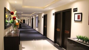 A hotel hallway with a long corridor, dark wooden doors, and a reception desk with a vase of flowers.