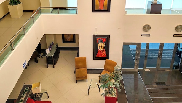 A multi-level hotel lobby with a glass railing, artwork on the walls, a seating area with sofas, and a staircase.