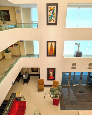 Et mereetages hotellobby med gelænder af glas, kunst på væggene, et loungeområde med sofaer og en trappe.