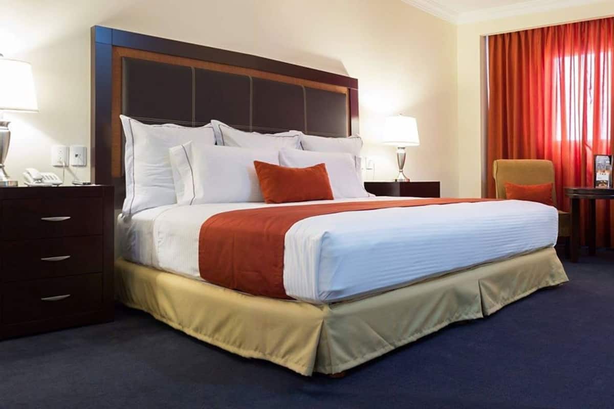 A hotel room with a large bed, two bedside tables, a chair, a desk, and a red curtain.