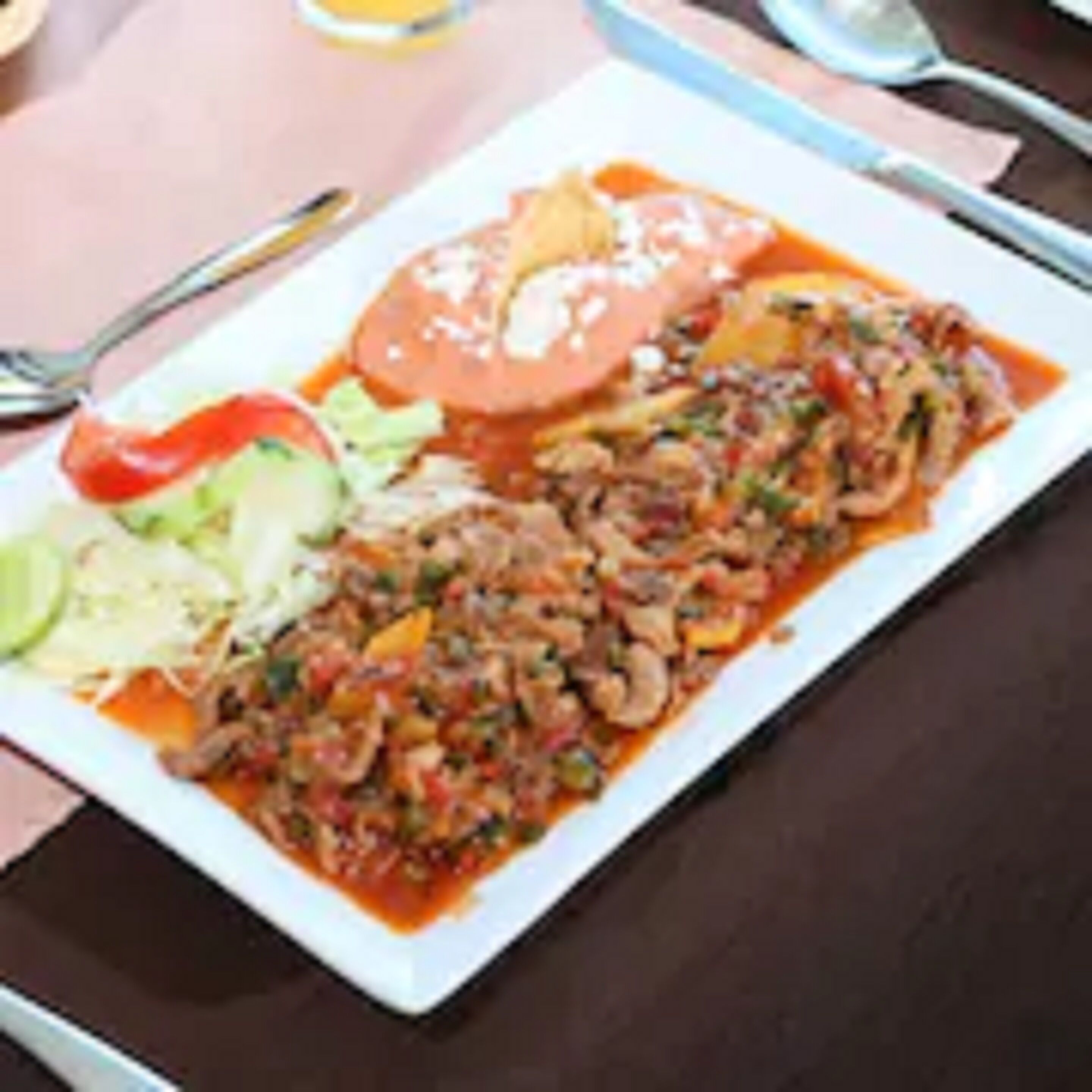 A rectangular plate with a dish that includes sliced meat, vegetables, and a tomato-based sauce.