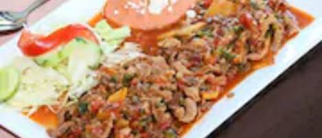 A rectangular plate with a dish that includes sliced meat, vegetables, and a tomato-based sauce.