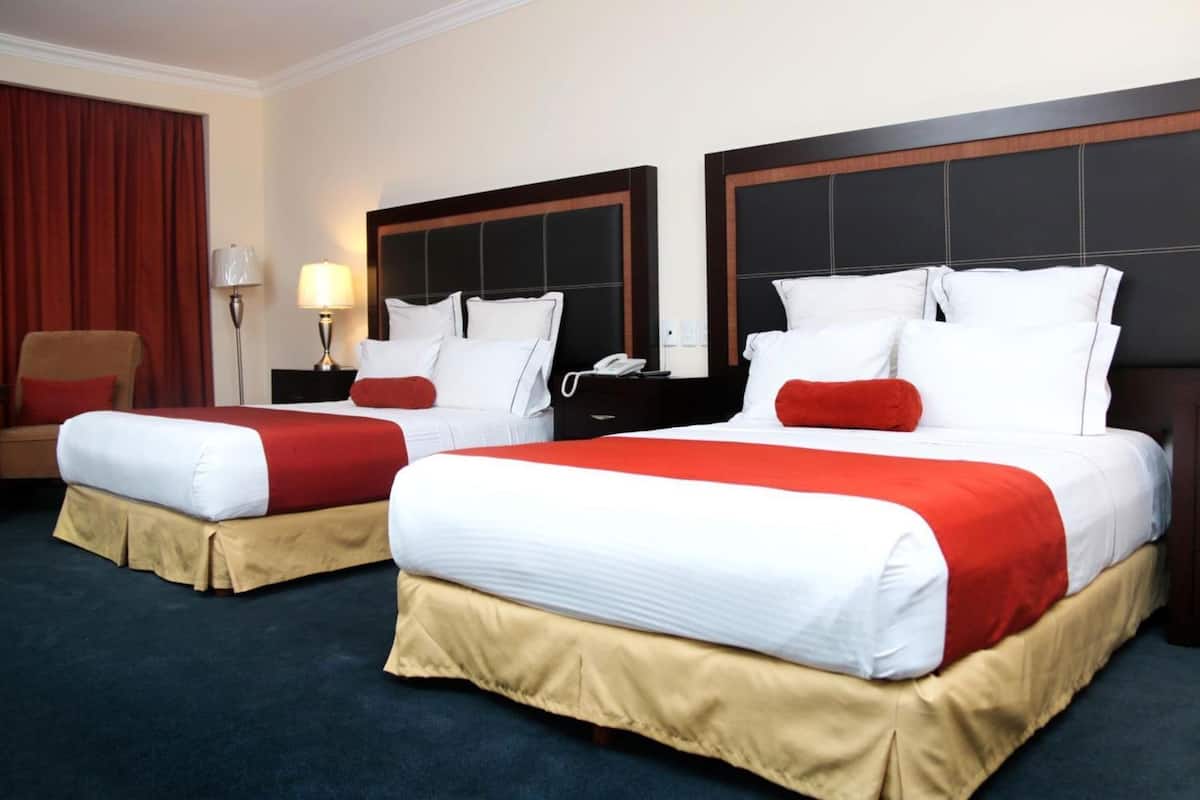 A hotel room with two beds, each with a red and white bedspread, a wooden headboard, and a nightstand with a lamp.