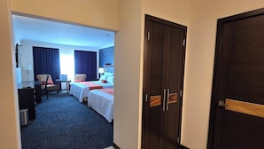A hotel room with a large bed, a desk, a chair, and a wardrobe.