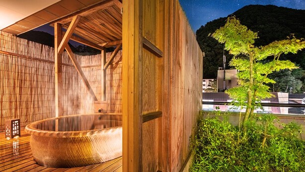 Un spa en bois doté d’un jacuzzi, de murs en bambou et offrant une vue sur le ciel nocturne.