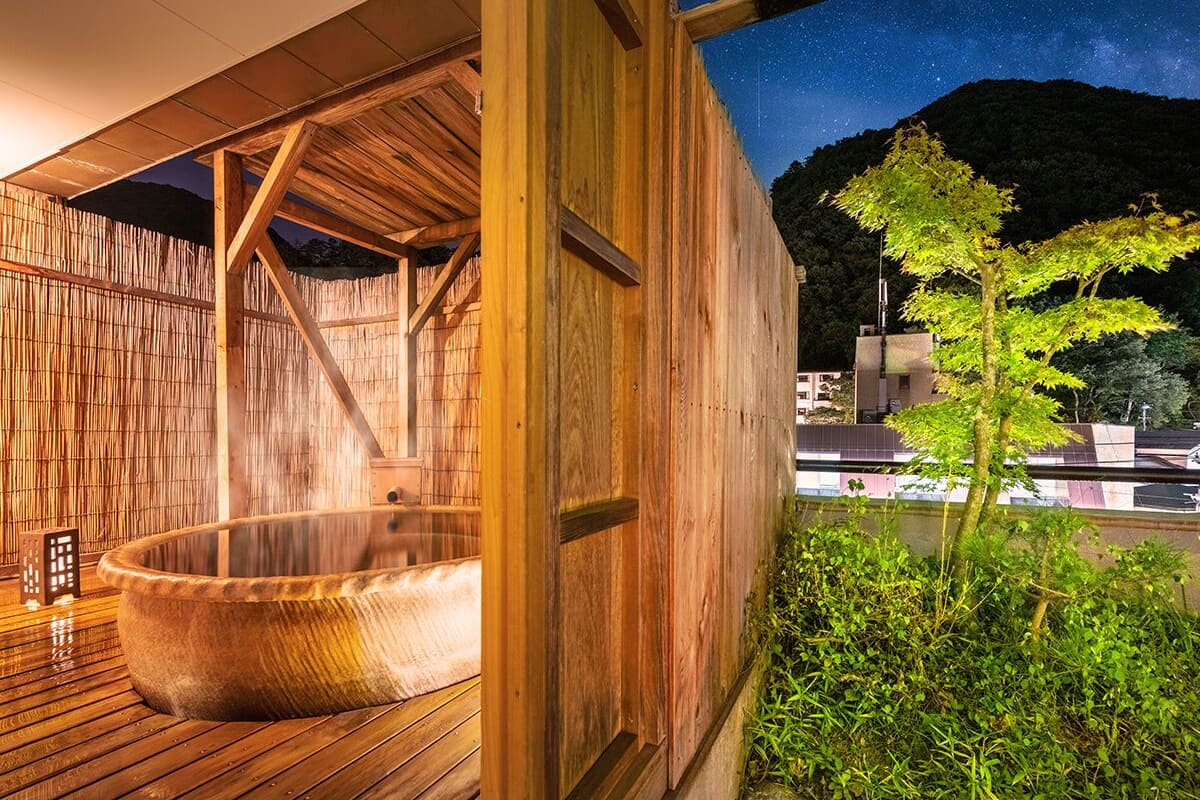 Un spa en bois doté d’un jacuzzi, de murs en bambou et offrant une vue sur le ciel nocturne.