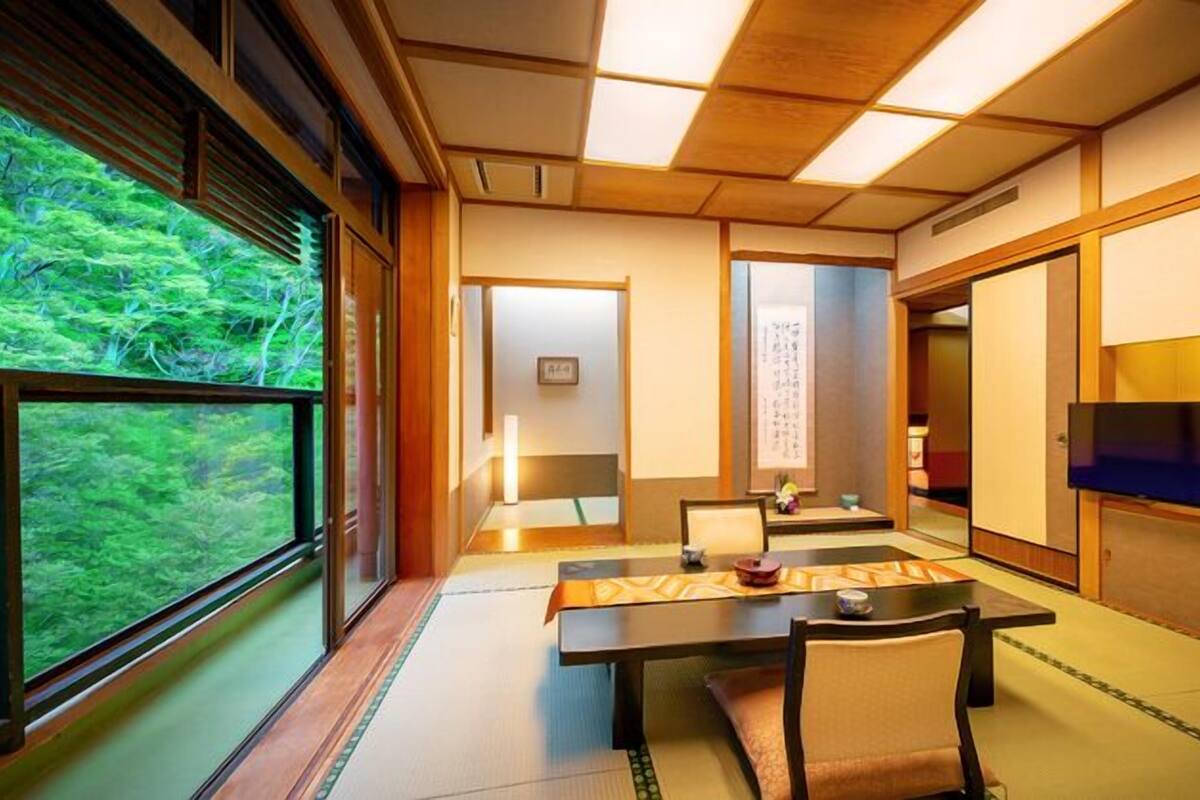Une pièce de style japonais traditionnel, avec un sol recouvert de tatamis, une petite table basse avec un coussin, un téléviseur et des portes coulissantes.