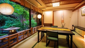 Une pièce de style japonais traditionnel, avec un sol recouvert de tatamis, une table basse et une vue sur un jardin luxuriant, visible à travers une porte coulissante.