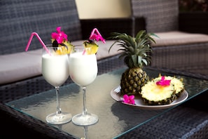 Two glasses of a white beverage with pink straws and garnishes, a pineapple, and a wicker table.