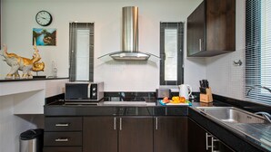 Una cocina moderna con armarios oscuros, una campana extractora de acero inoxidable, un microondas y un lavabo.