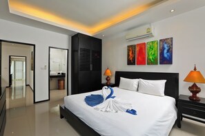 A hotel room with a bed, two bedside lamps, a wall-mounted air conditioner, and a hallway leading to another room. - Thaimond Residence by TropicLook (Rawai)