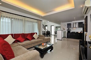 A modern living room with a sofa, coffee table, and a kitchen area in the background. - Thaimond Residence by TropicLook (Rawai)