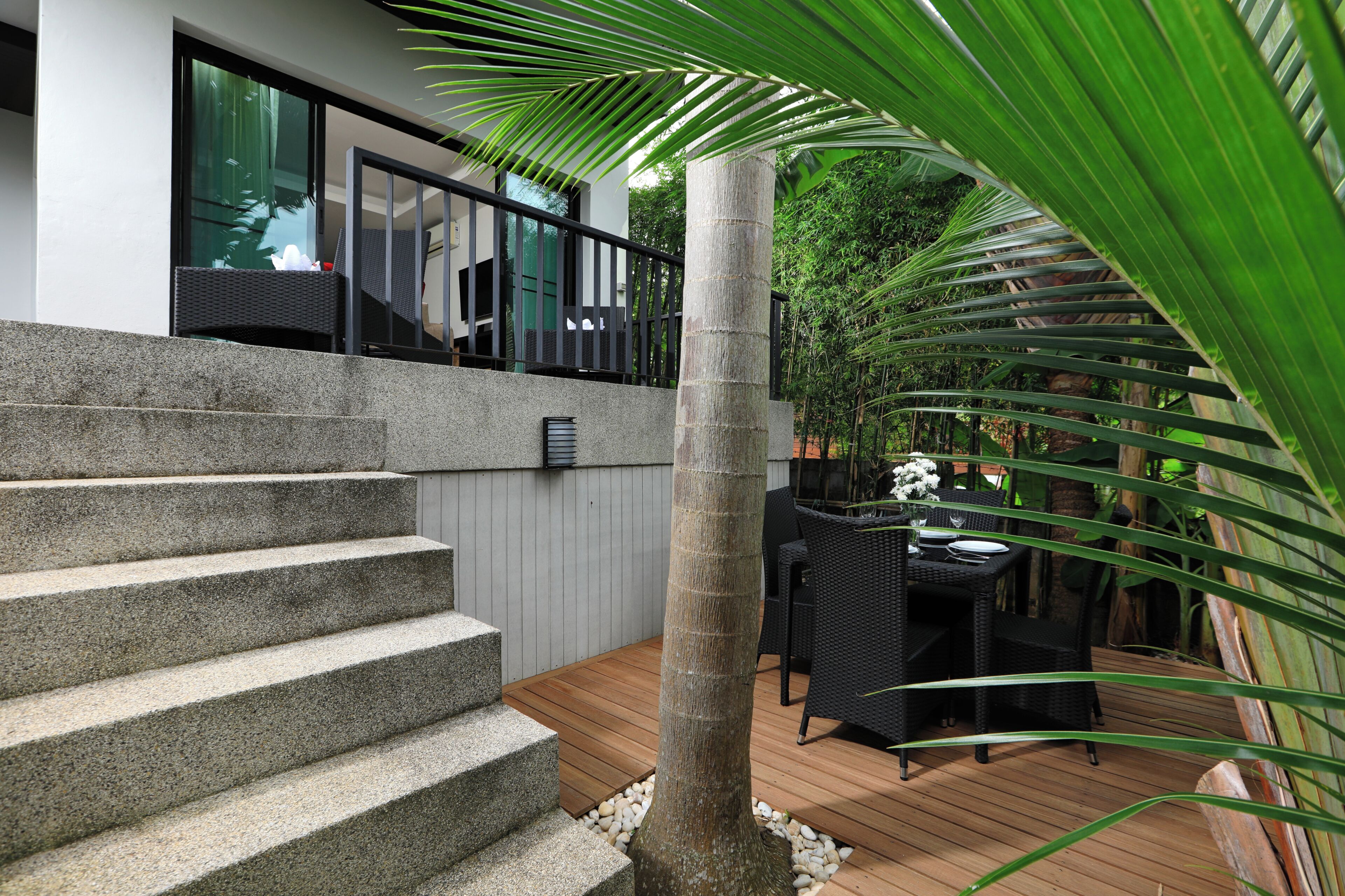 A modern outdoor staircase leading to a balcony with a view of a lush garden.