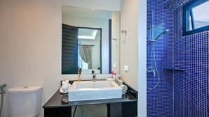 Un baño moderno con un lavabo blanco, encimera negra y zona de ducha con azulejos azules.