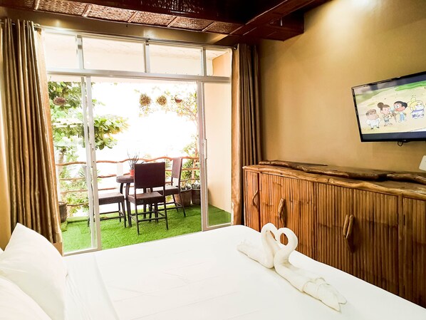 Una habitación de hotel con cama, televisión, aparador de madera y balcón con mesa y sillas.